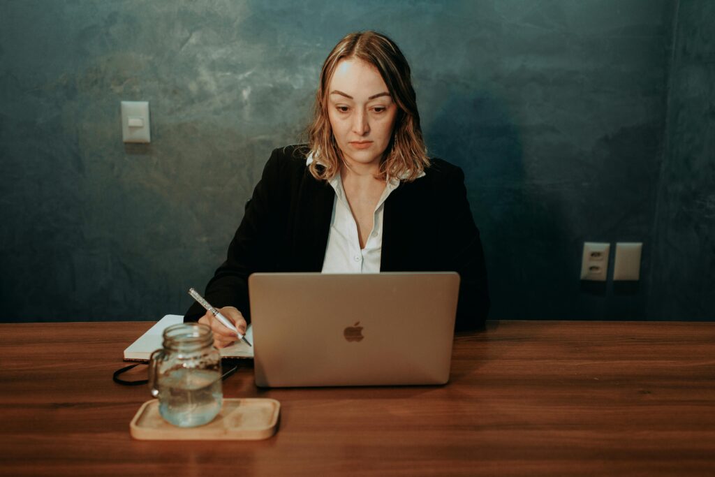 A woman writing and sitting at a table with her laptop