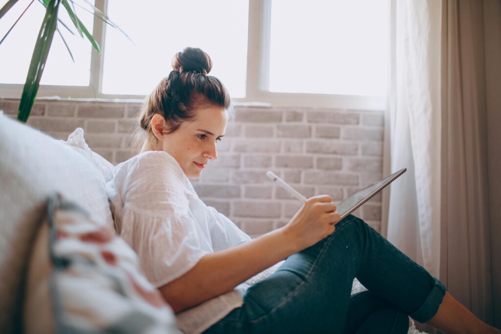 Woman writing and sitting on couch with tablet and pen