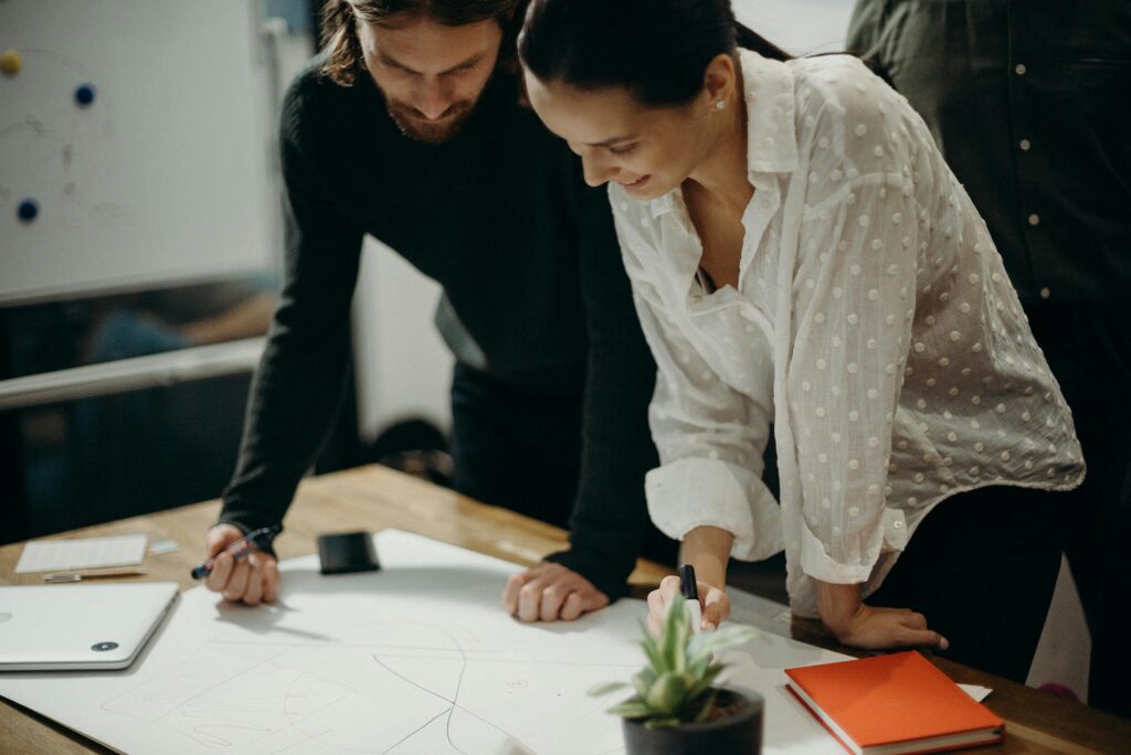 about Man and Woman Leaning on Table Staring at White Board on Top of Table Having a Meeting